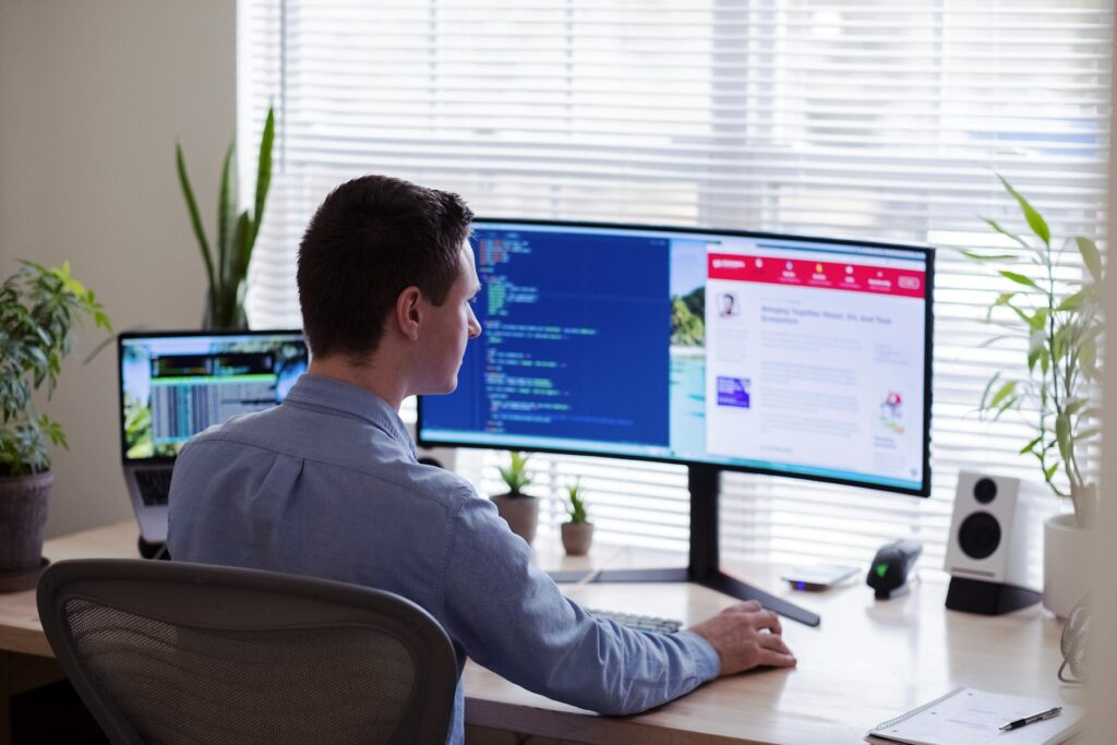 Webentwickler arbeitet an einem großen Monitor an einem hellen Schreibtisch