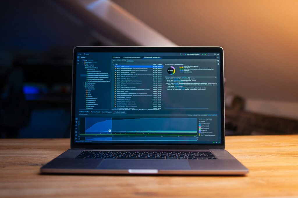 Laptop mit Code-Editor und Auswertungen auf einem Holzschreibtisch